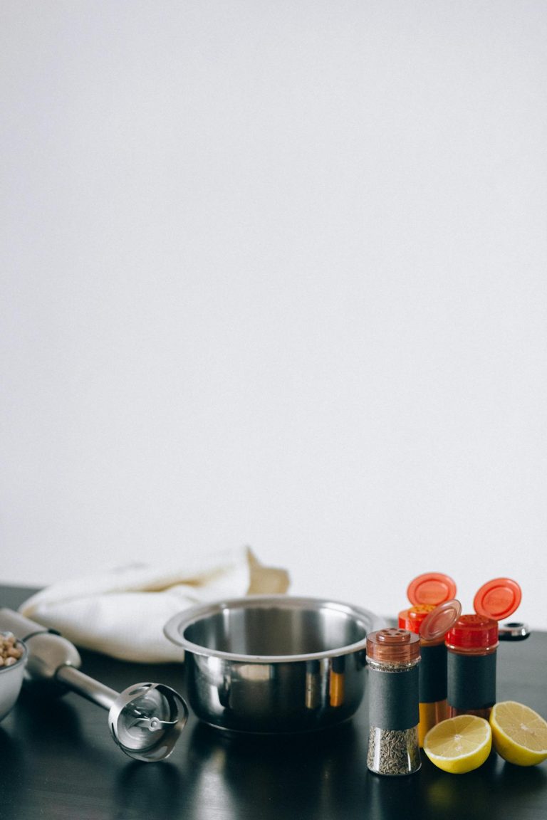 A minimalist kitchen scene with spices, a mixing bowl, and sliced lemons on a dark counter.