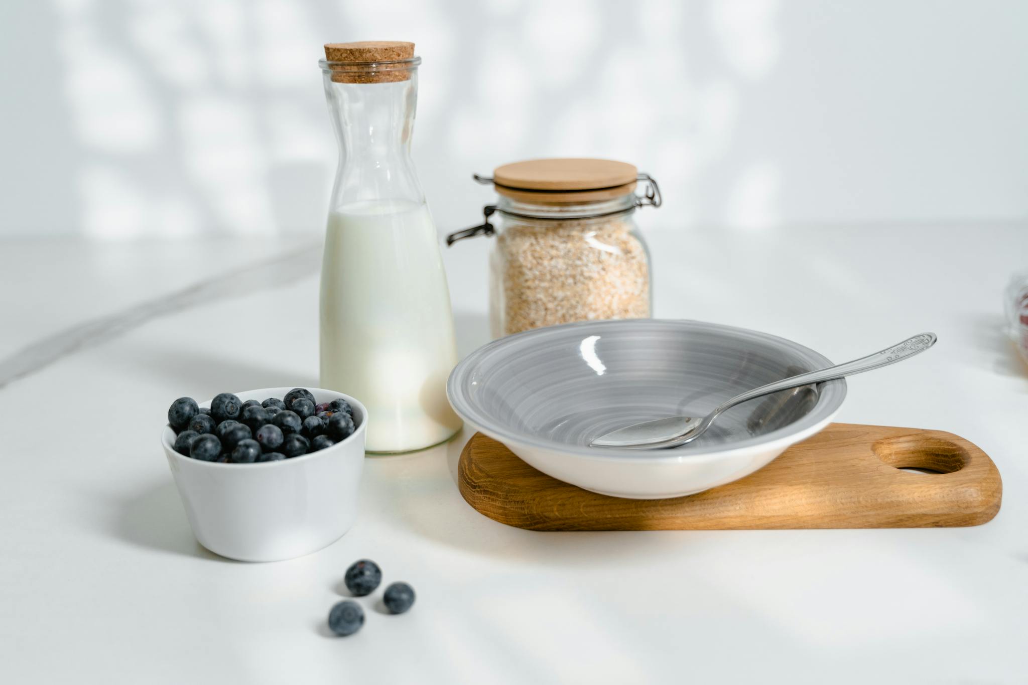 A minimalistic breakfast setup featuring blueberries, milk, and oats on a bright kitchen counter.